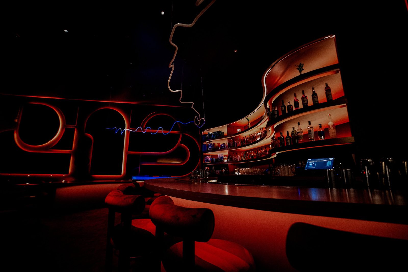 The curved bar at Alter Ego, with backlit shelves of bottles and red-lit stools in the foreground